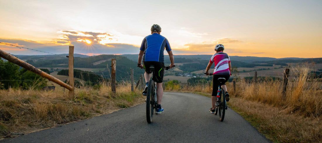 Fahrgemeinschaft: Zwei Radfahrer fahren bei Sonnenuntergang auf einer Straße mit Weitsicht