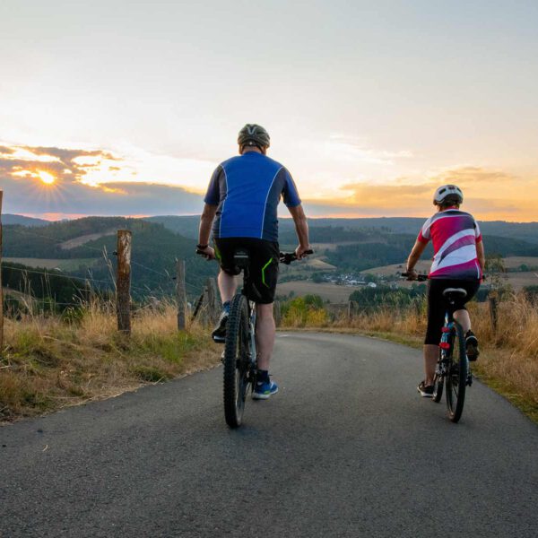 Fahrgemeinschaft: Zwei Radfahrer fahren bei Sonnenuntergang auf einer Straße mit Weitsicht