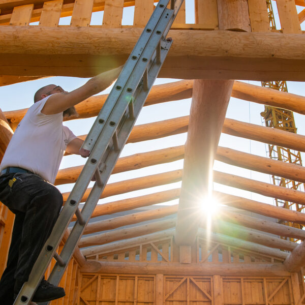 Zimmermann steigt mit einer Leiter auf das Dach eines Holzhauses