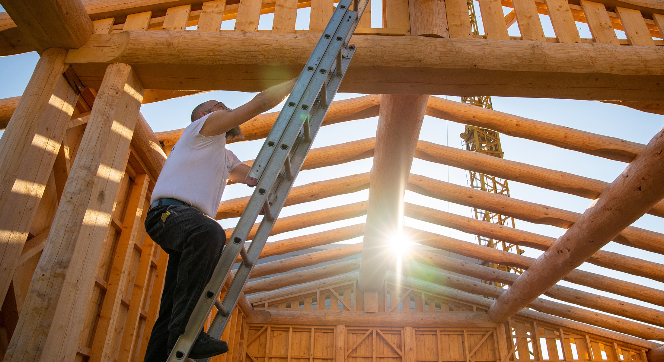 Zimmermann steigt mit einer Leiter auf das Dach eines Holzhauses