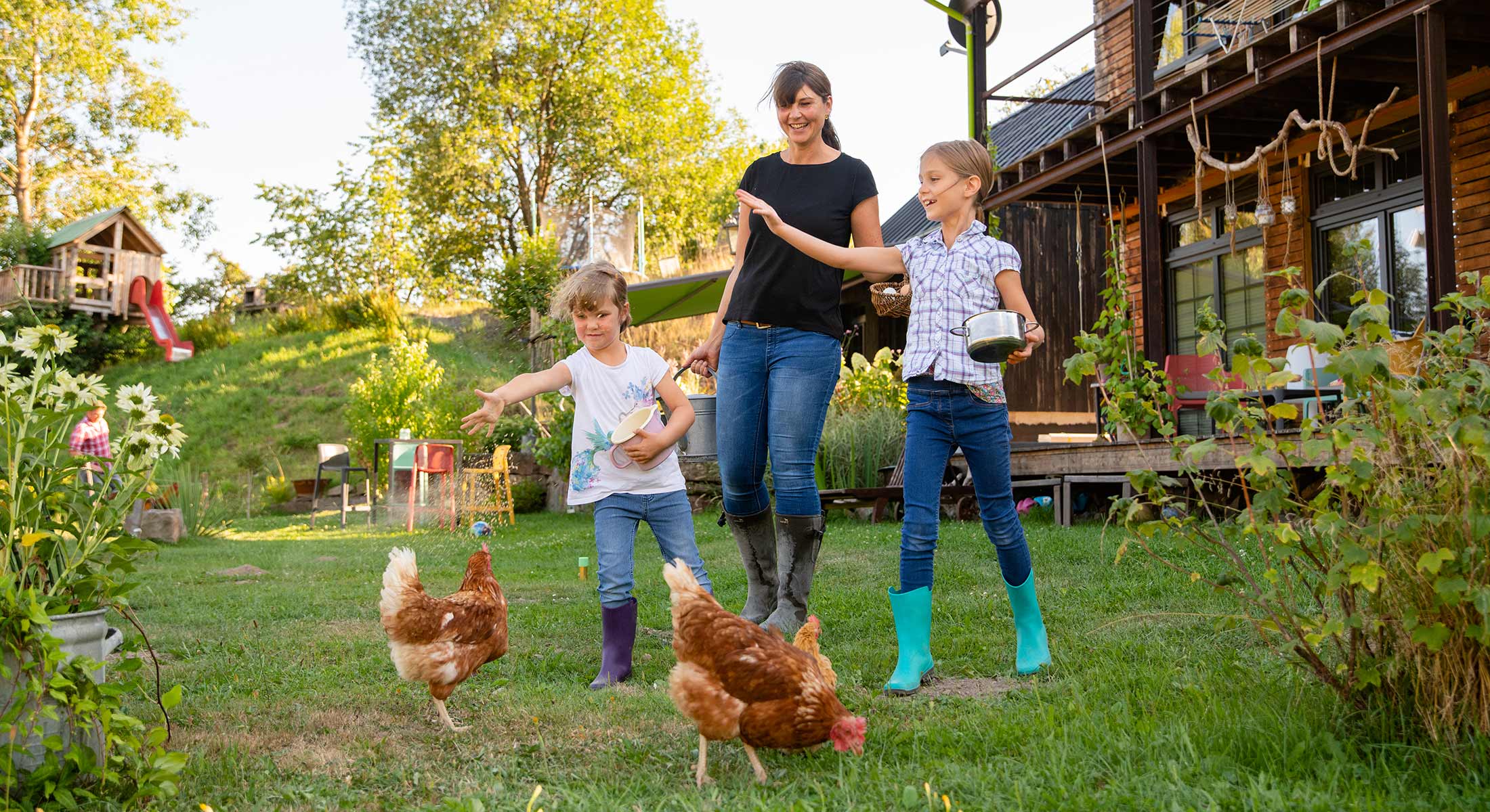 Eine Mutter mit ihren zwei kleinen Töchtern füttert Hühner im Garten