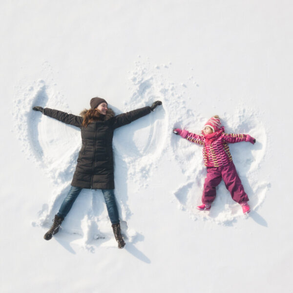 Das Weihnachtsmotiv der Einfach Ankommen Kampagne zeigt Mutter und Kind, die unbeschwert einen Schneeengel kreieren.